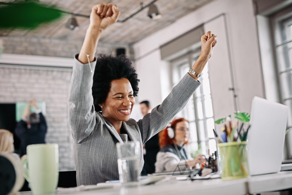 Low angle view of happy black businesswoman working in the office and celebrating her success with raised arms